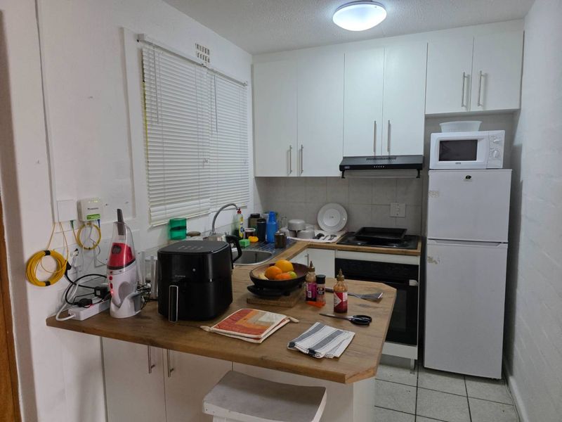 Compact kitchen featuring white cabinetry, wood-look countertop, built-in oven, hob, extractor fan, and tiled flooring.