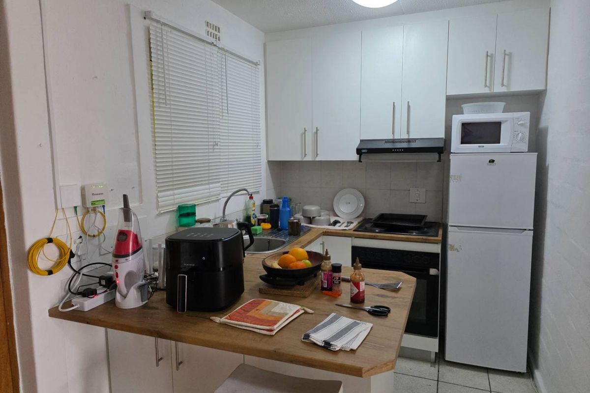 Compact kitchen featuring white cabinetry, wood-look countertop, built-in oven, hob, extractor fan, and tiled flooring.