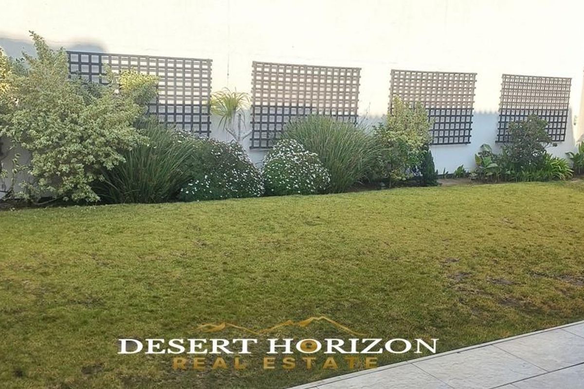 A well-maintained rear garden featuring a manicured lawn and decorative wall-mounted lattice panels against a clean exterior wall.