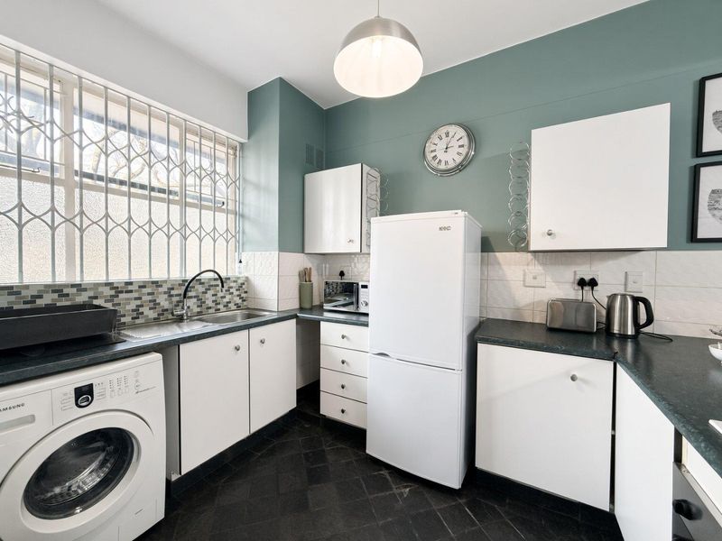 Functional kitchen featuring white cabinetry, dark countertops, tiled backsplash, and integrated laundry plumbing, finished with a modern teal accent wall.