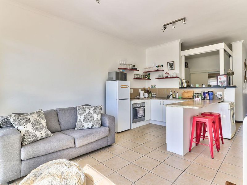Open-plan living and kitchen area featuring tiled flooring, built-in cabinetry, a breakfast bar, and floating shelving in a functional layout.