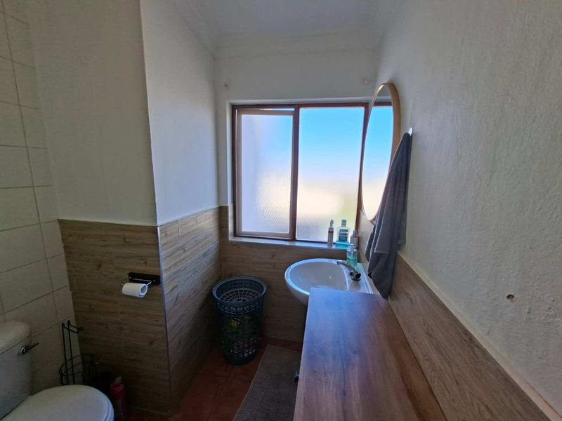 A compact bathroom featuring wood-look wall tiling, a pedestal basin, and a sliding window providing natural light.