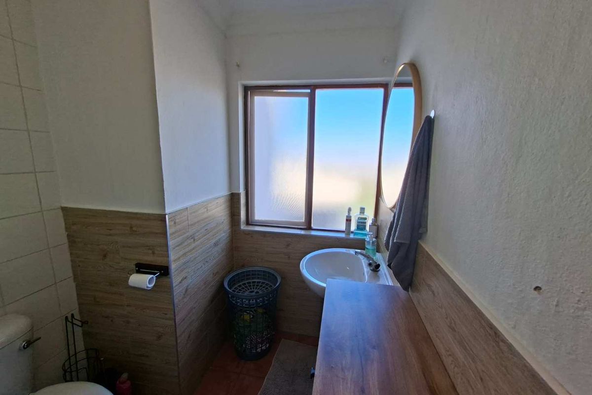 A compact bathroom featuring wood-look wall tiling, a pedestal basin, and a sliding window providing natural light.