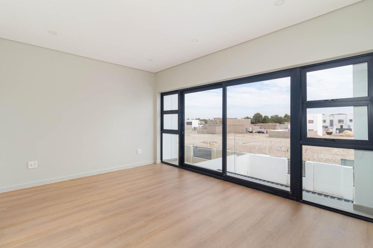 A bright, empty bedroom featuring modern light wood-look flooring, neutral walls, and large black-framed sliding glass doors leading to an outdoor area.