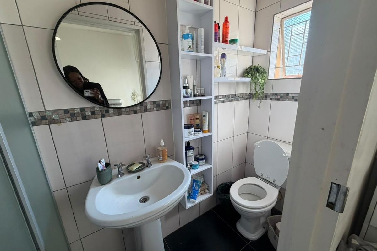 A compact bathroom featuring a pedestal basin, toilet, tiled walls with decorative mosaic accents, and built-in vertical shelving.