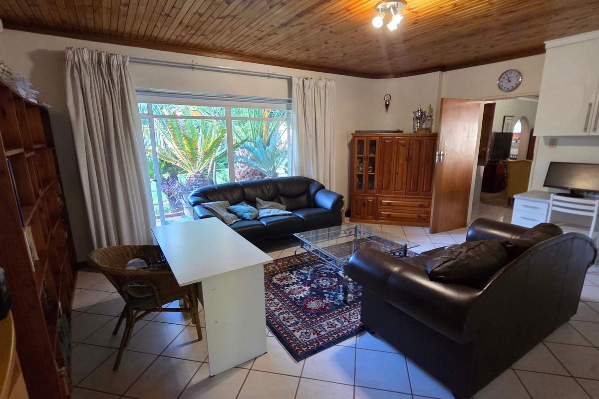 A spacious living room featuring a timber-clad ceiling, tiled flooring, and large sliding glass doors providing natural light and garden views.