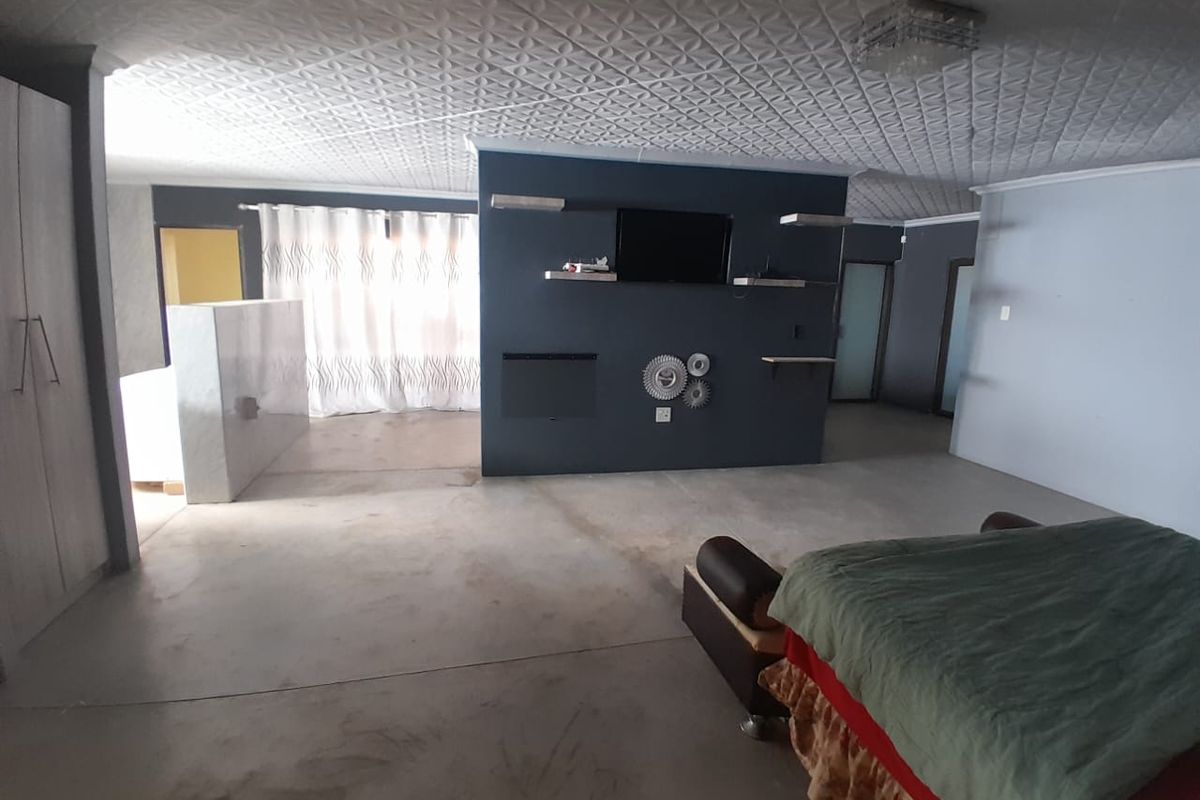 Spacious bedroom featuring a central partition wall with built-in shelving and a textured ceiling, requiring floor refinishing to enhance the space.