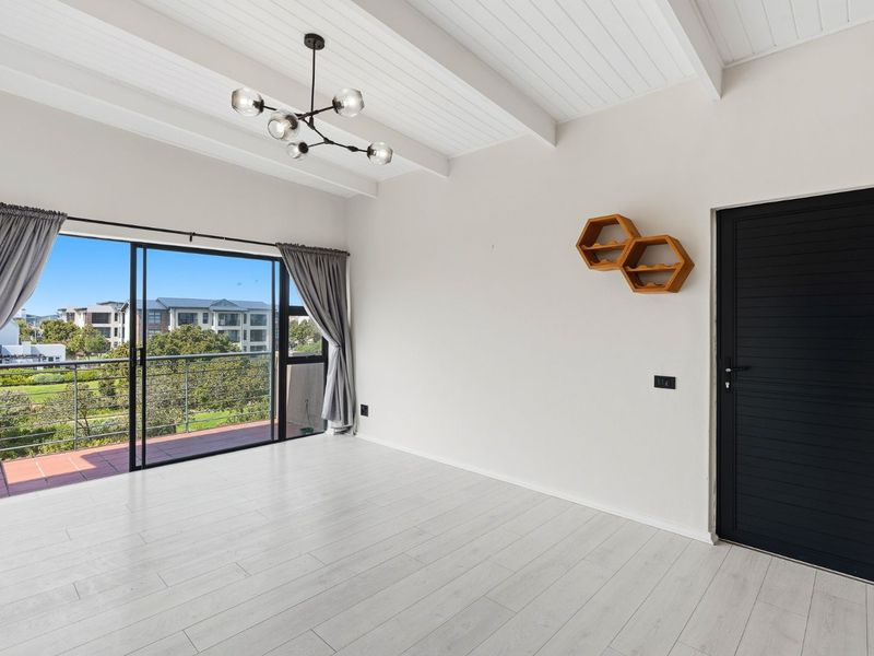 Bright and spacious living area featuring exposed beam ceilings, modern laminate flooring, and large sliding glass doors leading to a private balcony.