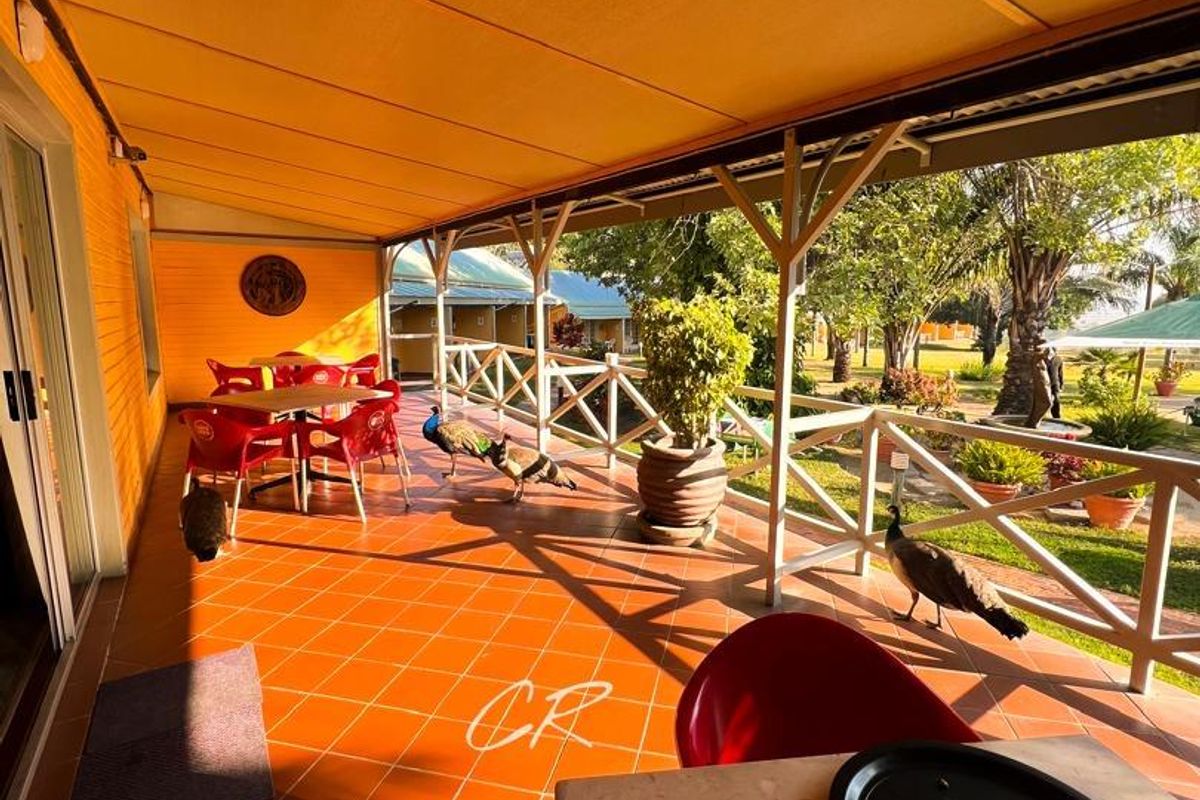 A covered outdoor patio area featuring tiled flooring and a timber balustrade, overlooking the hotel grounds.
