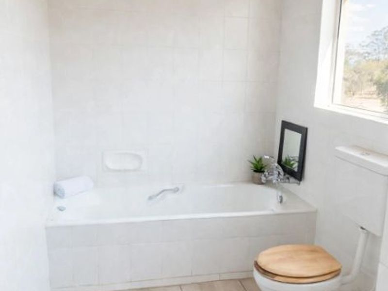A clean bathroom featuring a built-in bathtub, toilet, tiled finishes, and a distinctive timber-paneled ceiling, offering a functional and bright space.