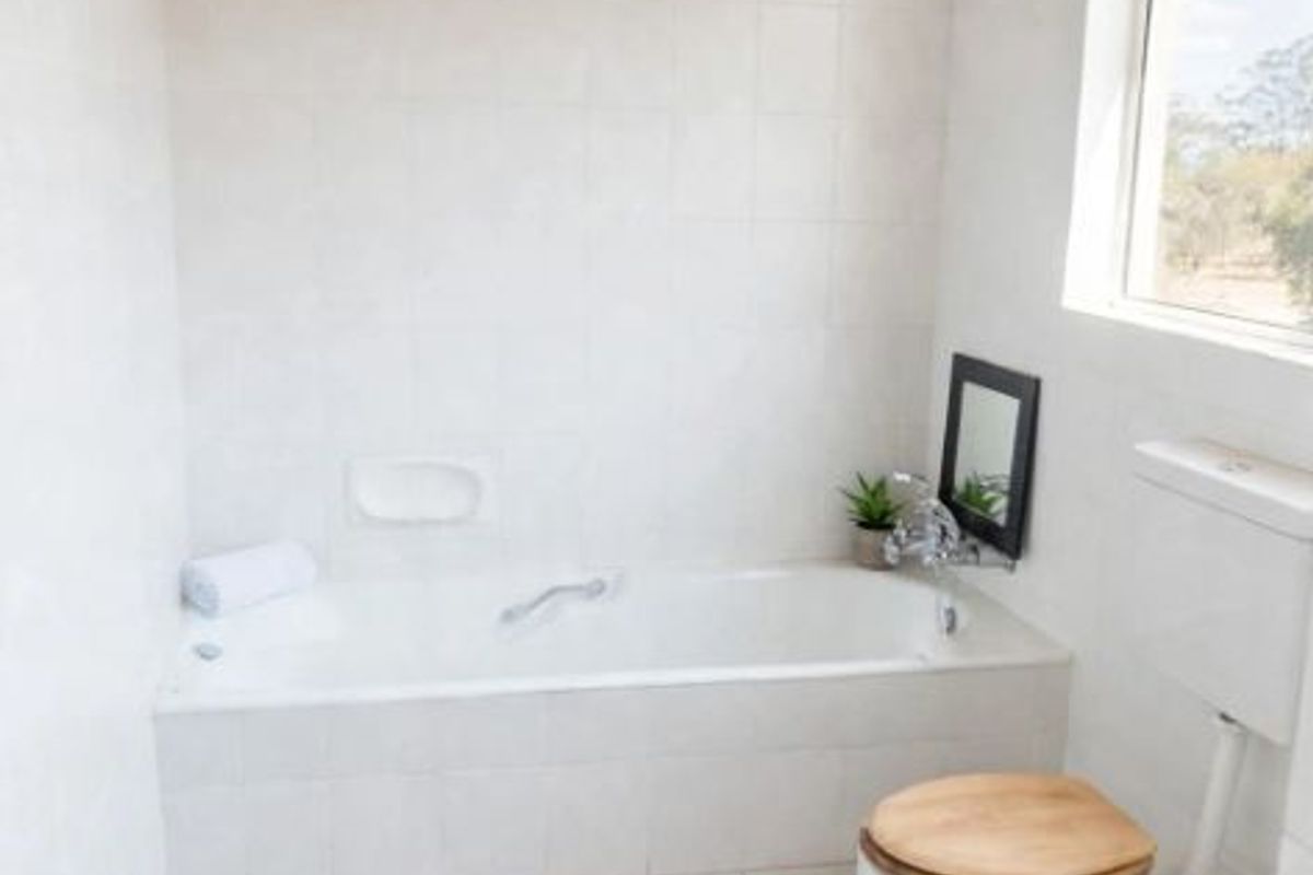 A clean bathroom featuring a built-in bathtub, toilet, tiled finishes, and a distinctive timber-paneled ceiling, offering a functional and bright space.