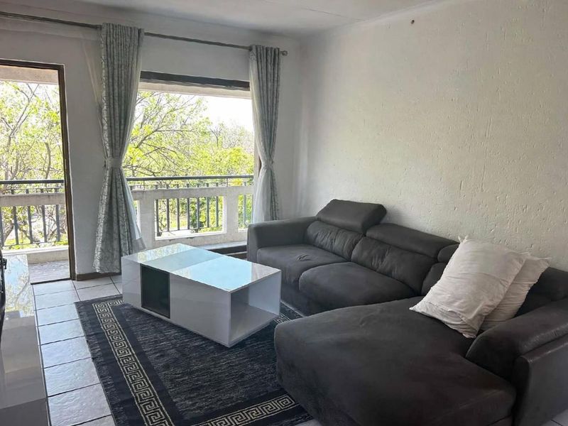 A living room featuring tiled flooring and direct access to a balcony through a sliding glass door, offering natural light and outdoor views.
