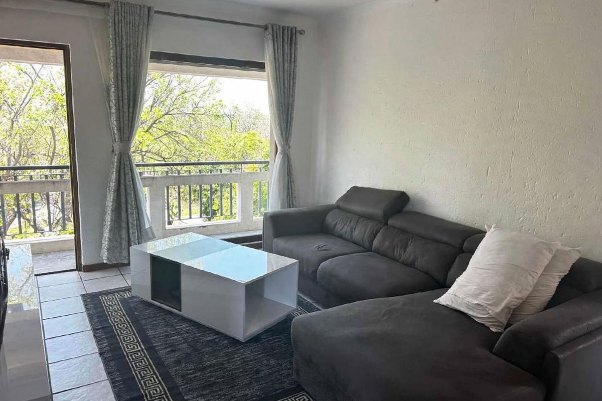 A living room featuring tiled flooring and direct access to a balcony through a sliding glass door, offering natural light and outdoor views.