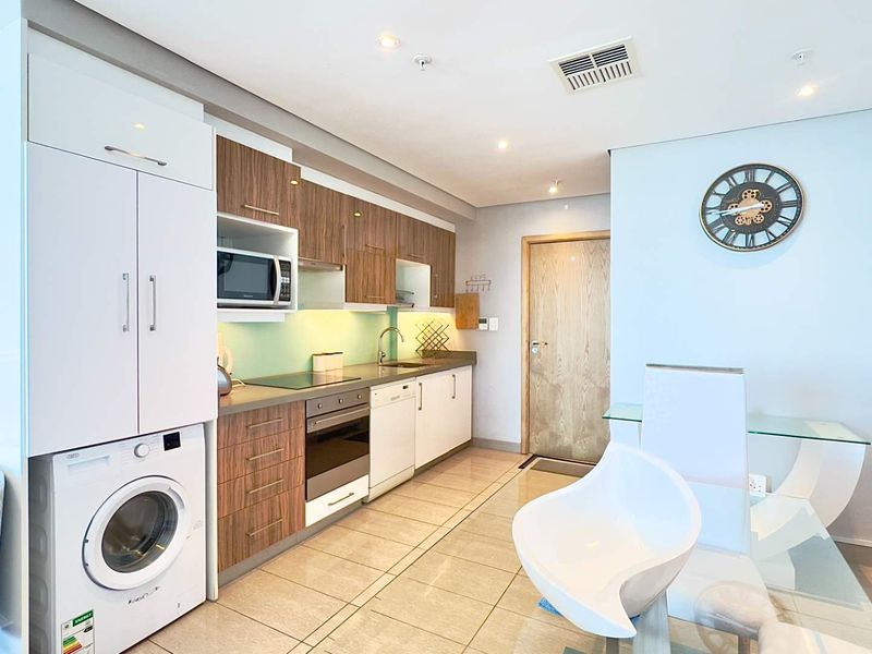 Modern kitchen featuring integrated appliances, wood-finish cabinetry, sleek countertops, and tiled flooring, seamlessly integrated into an open-plan living space.