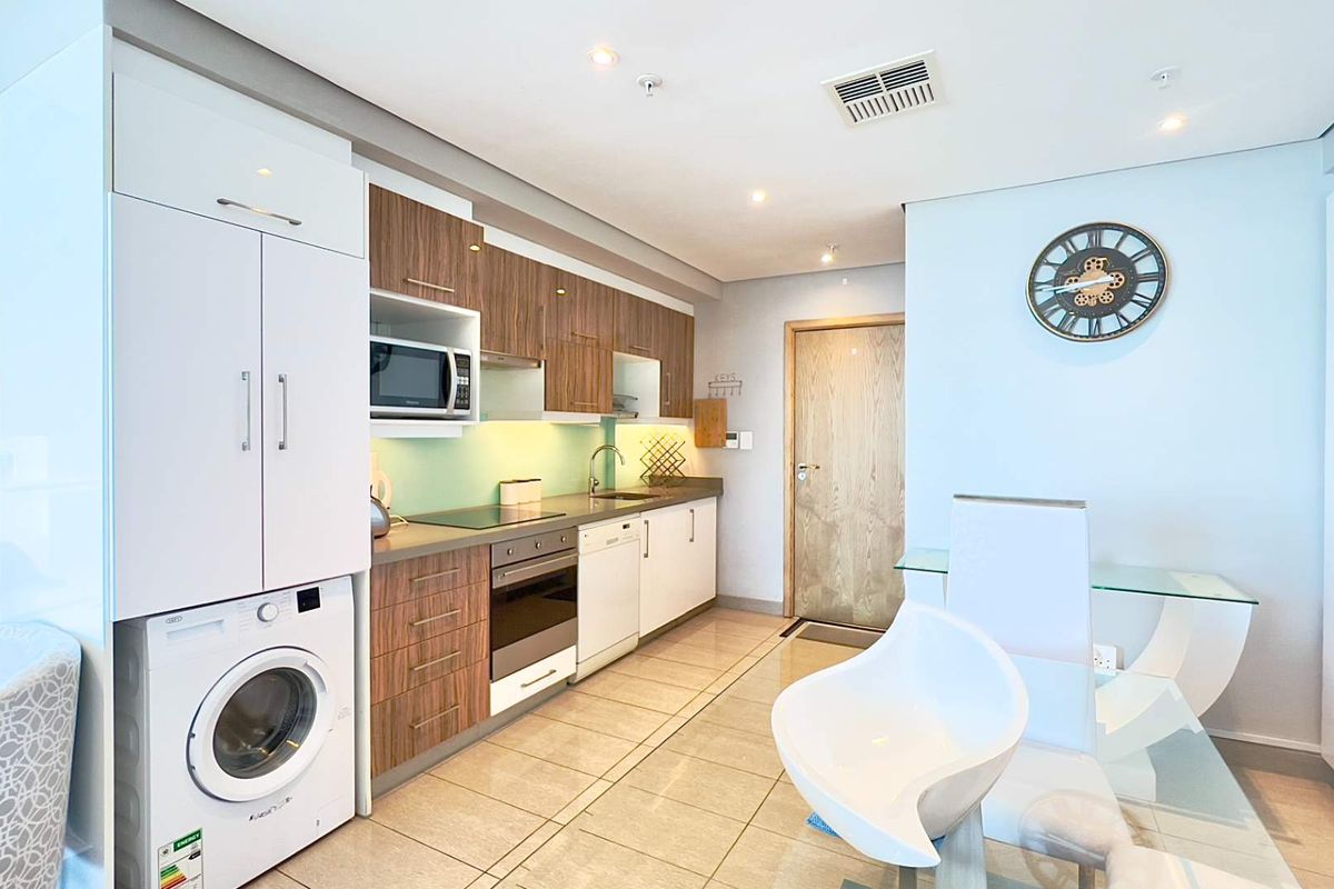 Modern kitchen featuring integrated appliances, wood-finish cabinetry, sleek countertops, and tiled flooring, seamlessly integrated into an open-plan living space.