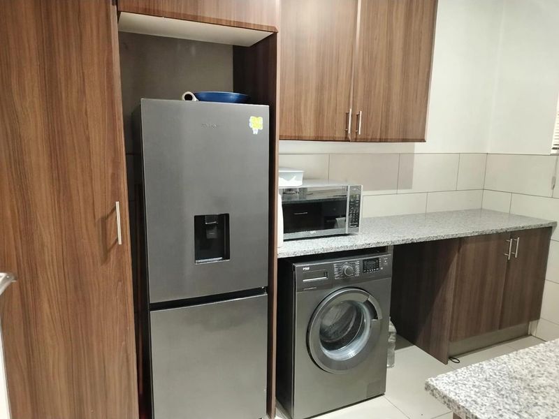 A functional kitchen area featuring wood-look laminate cabinetry, granite countertops, and a tiled backsplash with dedicated space for appliances.
