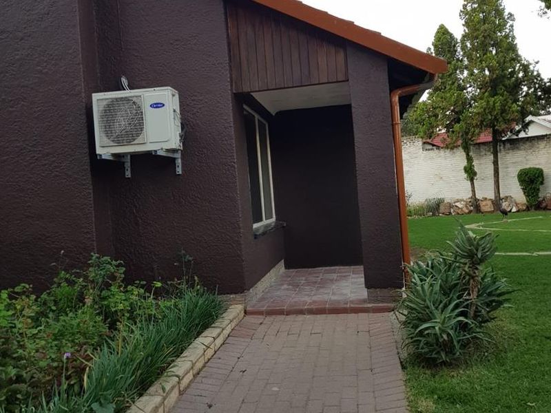A view of the rear exterior featuring a paved walkway leading to a covered patio area with an installed air conditioning unit.