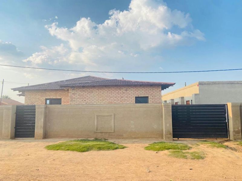 Front view of a facebrick house featuring a perimeter wall with dual metal gates and a tiled roof.
