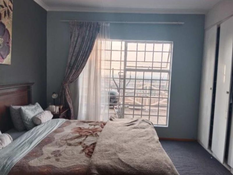A bedroom featuring built-in cupboards and a large window with security bars, offering natural light and a view.