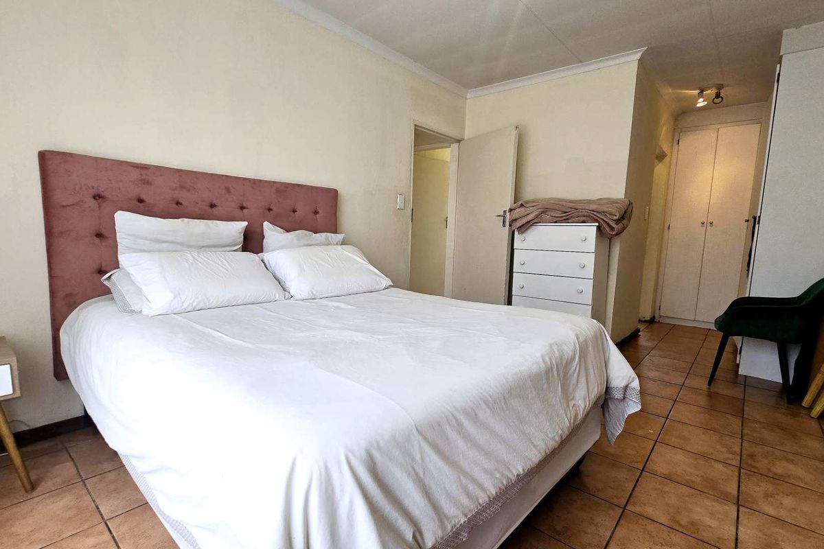 A bedroom featuring tiled flooring, built-in cupboards, and neutral wall finishes, providing a functional and well-lit sleeping space.
