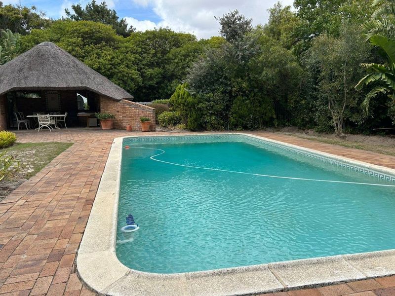 Outdoor pool area featuring a swimming pool, brick paved surround, and a traditional thatched lapa for shaded outdoor entertainment.