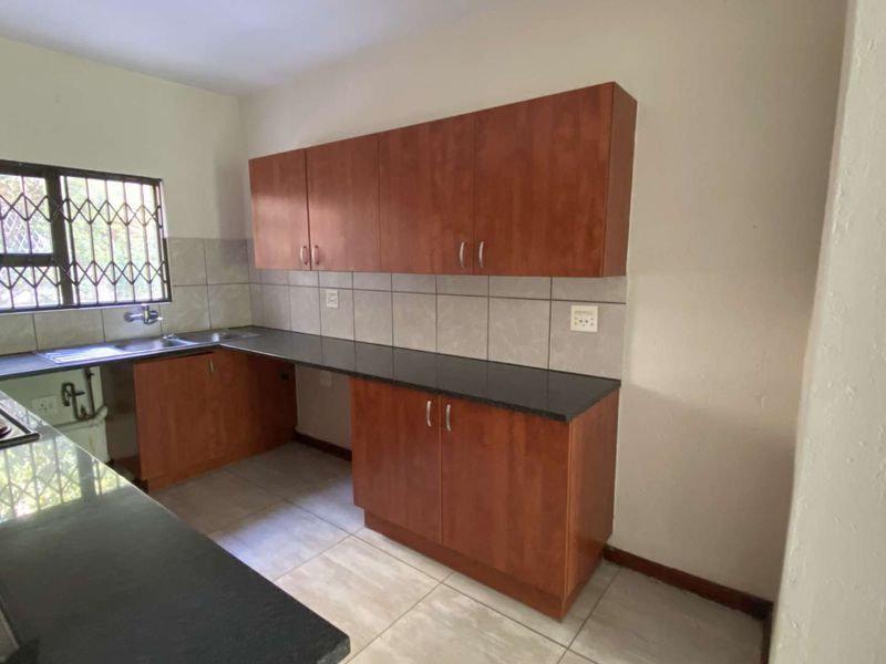 A functional kitchen featuring laminate cabinetry, granite countertops, a stainless steel sink, and ceramic tile flooring with security bars on the window.