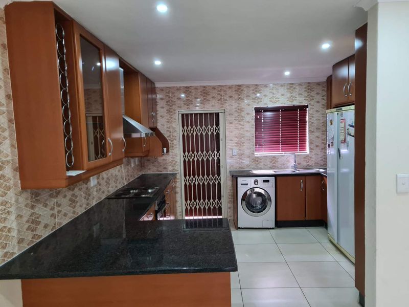 A functional kitchen featuring dark granite countertops, wood-finish cabinetry, tiled backsplash, and integrated appliances, with a security gate leading to the exterior.