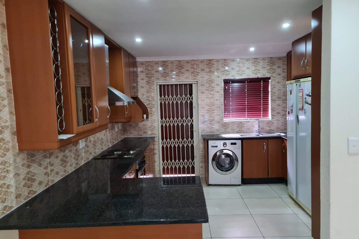 A functional kitchen featuring dark granite countertops, wood-finish cabinetry, tiled backsplash, and integrated appliances, with a security gate leading to the exterior.