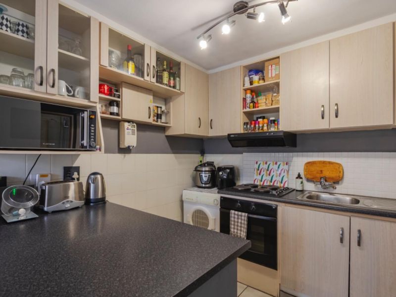 A functional kitchen featuring light wood-tone cabinetry, dark laminate countertops, a built-in oven with hob, and a tiled backsplash.