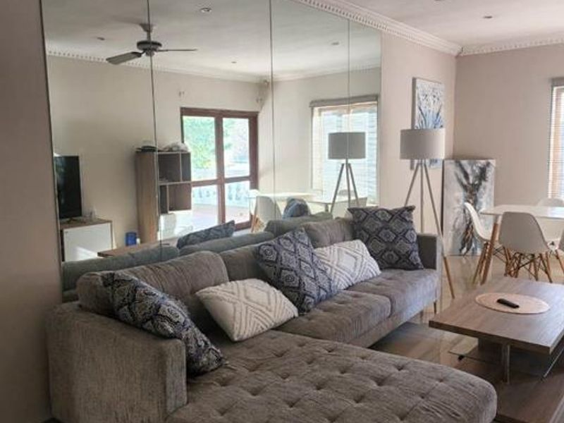 A spacious living room featuring a large floor-to-ceiling mirrored wall, tiled flooring, and crown molding, creating a bright and open atmosphere.