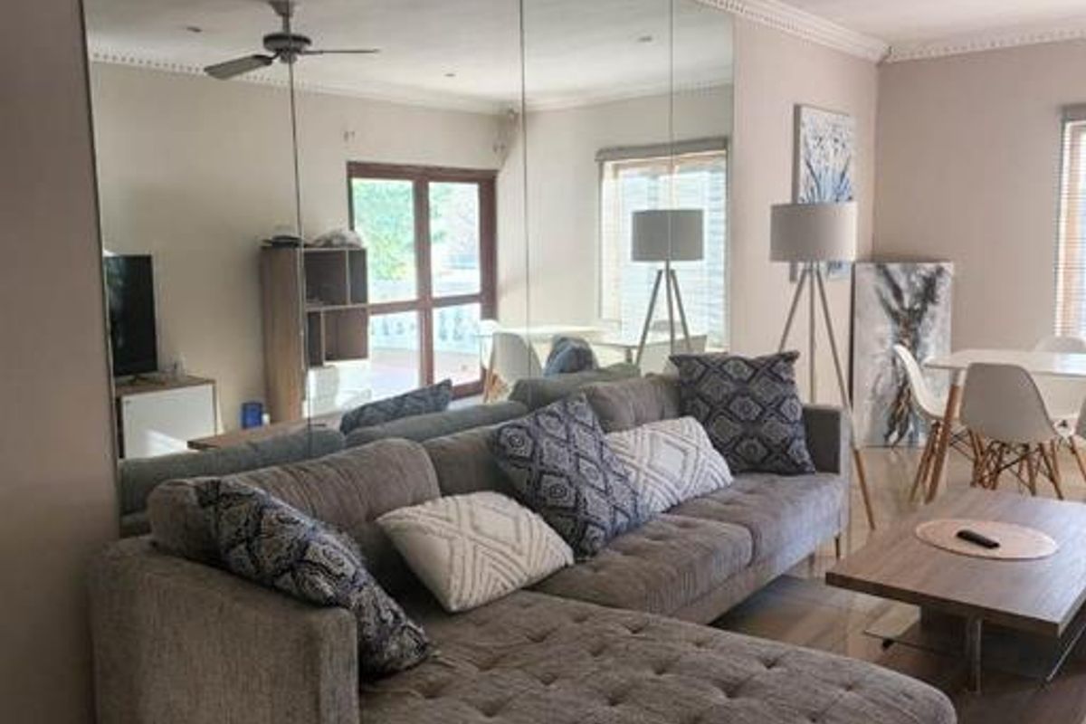 A spacious living room featuring a large floor-to-ceiling mirrored wall, tiled flooring, and crown molding, creating a bright and open atmosphere.