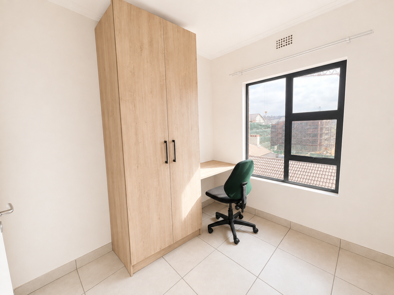 A bright bedroom featuring neutral tiled flooring, a modern light wood built-in wardrobe, an integrated desk, and a large window with aluminium frames.
