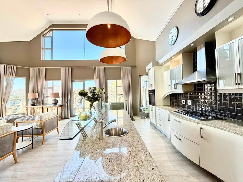 Spacious open-plan kitchen and living area featuring a large granite island, modern built-in appliances, vaulted ceilings, and expansive windows with natural light.