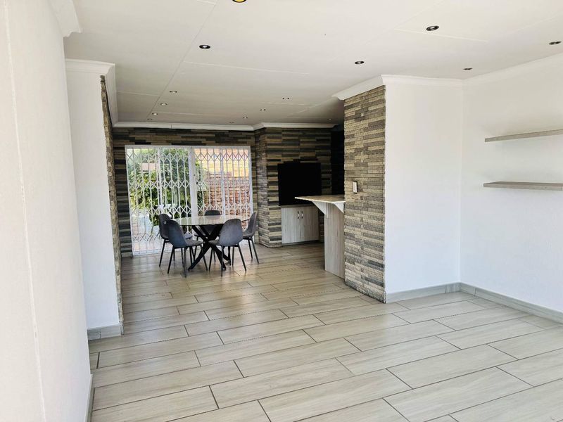 Spacious open-plan living area featuring modern tiled flooring, stone-clad accent walls, recessed lighting, and a built-in breakfast bar with direct access to the exterior.