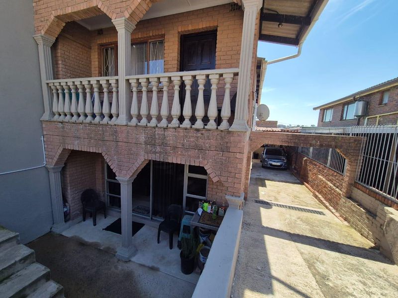 Rear view of a two-story brick house featuring a covered patio, upper-level balcony with balustrade, and a paved driveway with a carport.