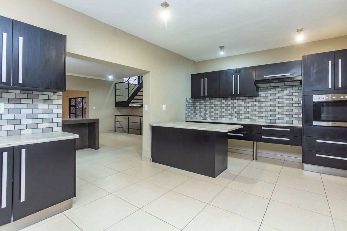 Modern kitchen featuring dark cabinetry, subway tile backsplash, built-in oven, and a central island, seamlessly flowing into the adjacent living area.