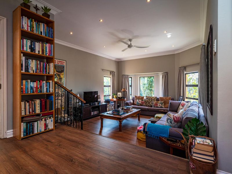 Spacious living room featuring warm laminate flooring, recessed downlights, a ceiling fan, and a wrought iron staircase railing leading to the upper level.