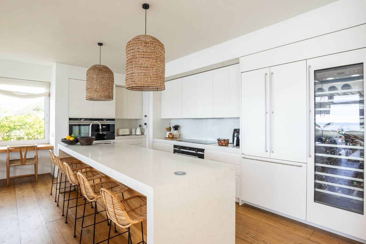 Modern kitchen featuring a large stone-topped island, integrated appliances, sleek white cabinetry, and warm timber flooring.