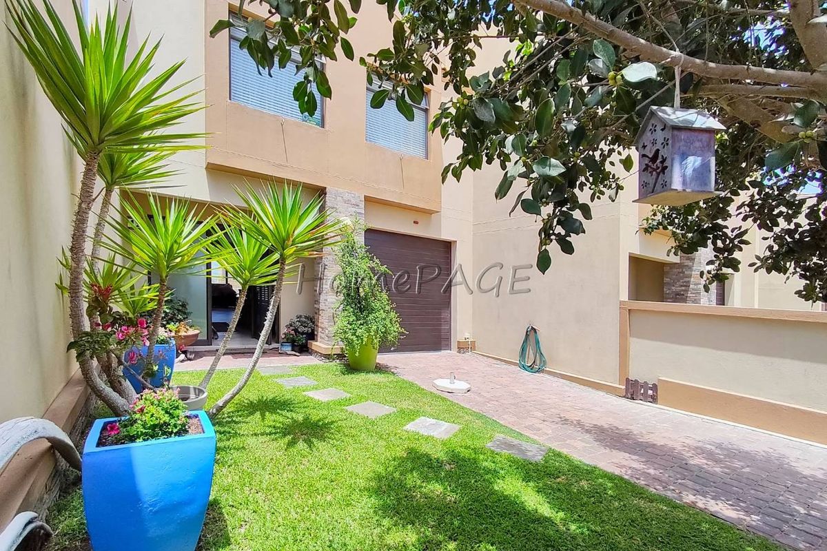 A view of the rear exterior of the townhouse, featuring a paved driveway, a small lawn area, and access to the garage.