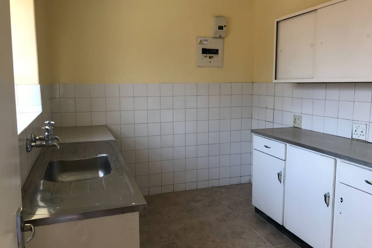 A functional, empty kitchen space featuring a stainless steel sink, tiled splashback, and built-in cabinetry with laminate countertops.