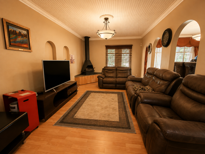 A cozy living room featuring a freestanding fireplace, beadboard ceiling, and distinctive arched wall openings, finished with laminate flooring.