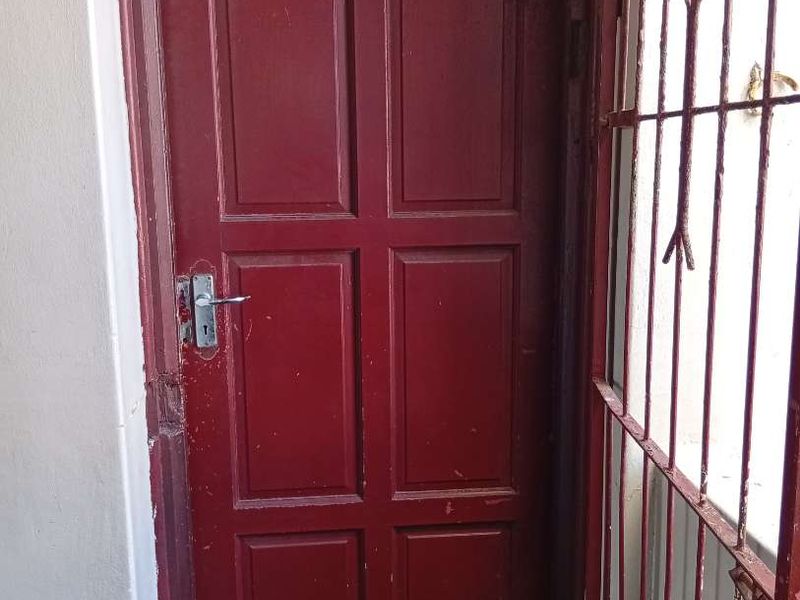 Apartment entrance featuring a solid timber door with a security gate and transom window, showing signs of wear and paint deterioration.