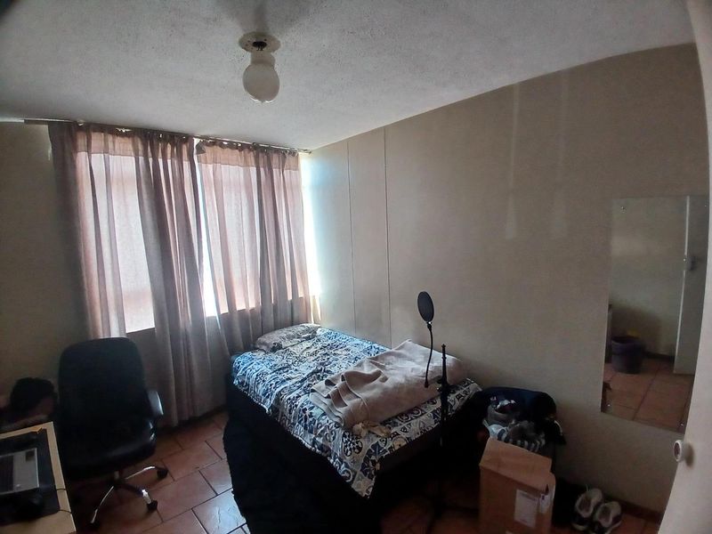 A bedroom featuring tiled flooring and large windows with curtain rails, requiring cosmetic updates to the ceiling and wall finishes.