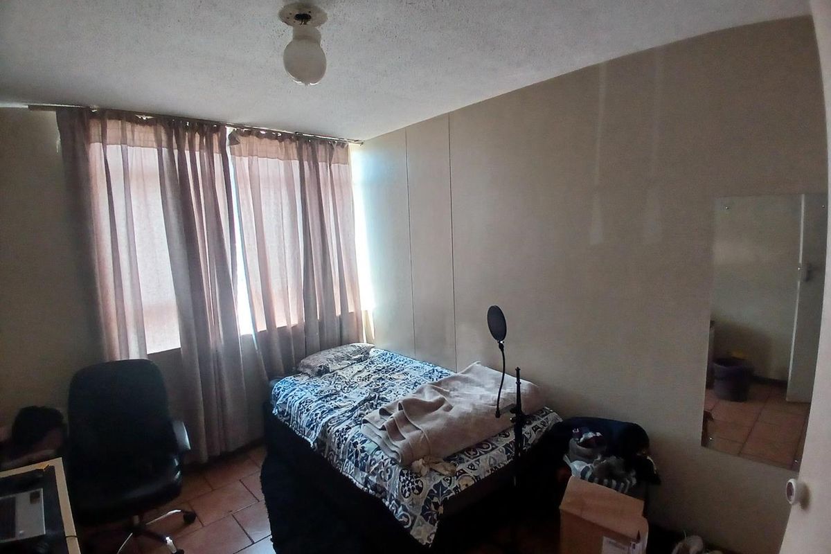 A bedroom featuring tiled flooring and large windows with curtain rails, requiring cosmetic updates to the ceiling and wall finishes.