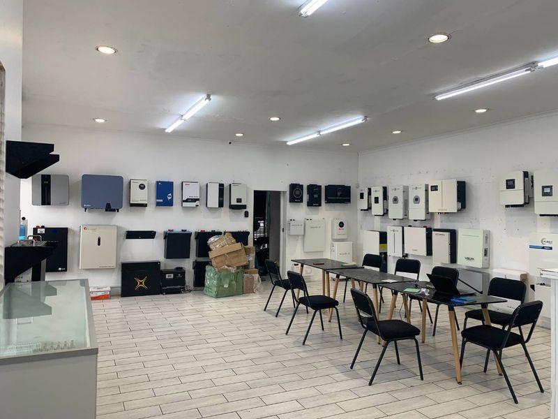A commercial utility space featuring wall-mounted solar inverters and battery storage systems, with tiled flooring and integrated lighting throughout.