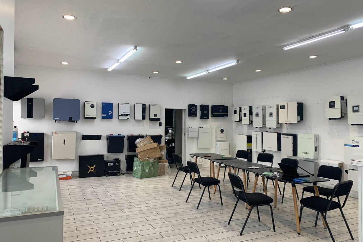 A commercial utility space featuring wall-mounted solar inverters and battery storage systems, with tiled flooring and integrated lighting throughout.