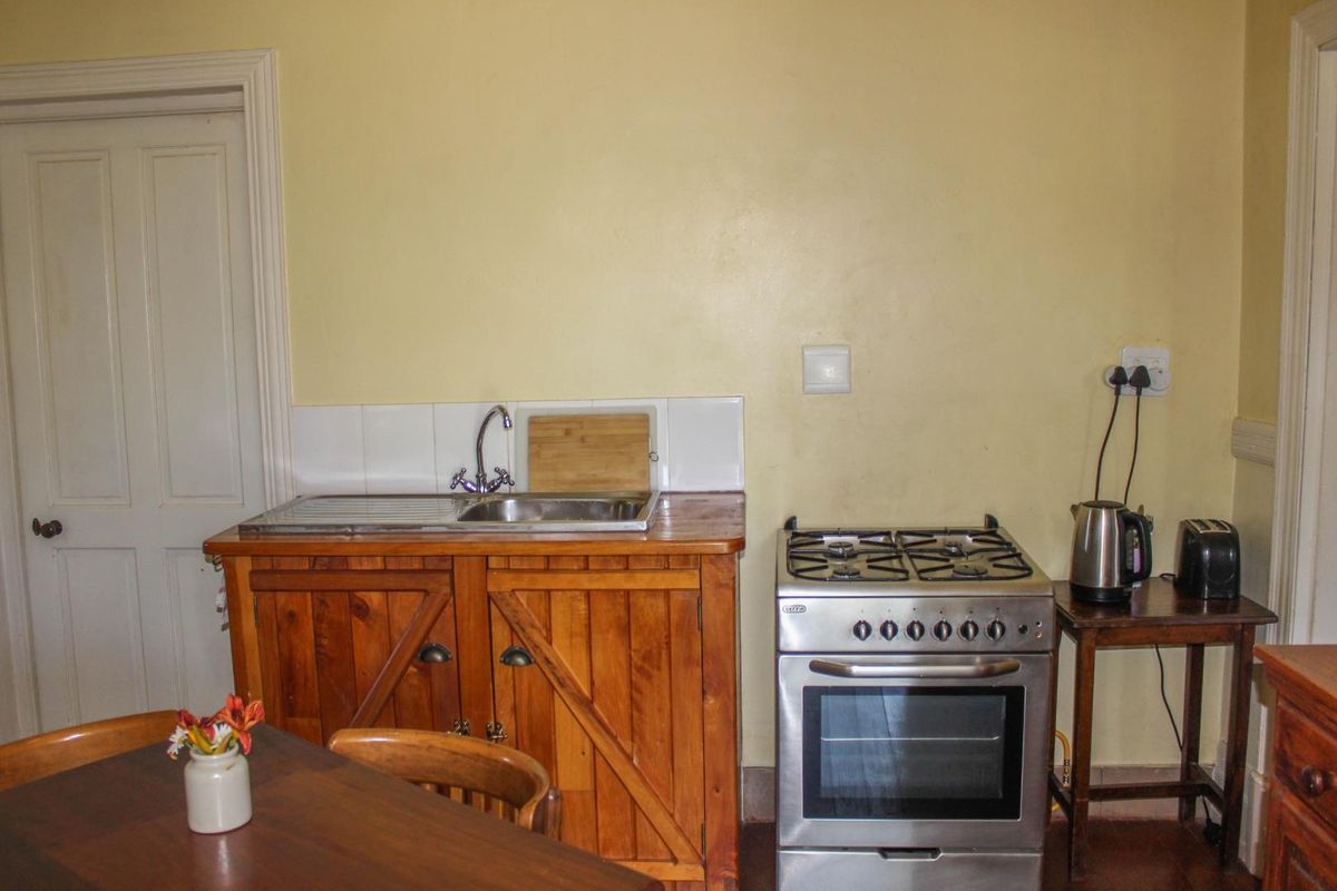 A compact kitchen area featuring wooden cabinetry, a stainless steel sink, and a freestanding gas stove with a tiled splashback.