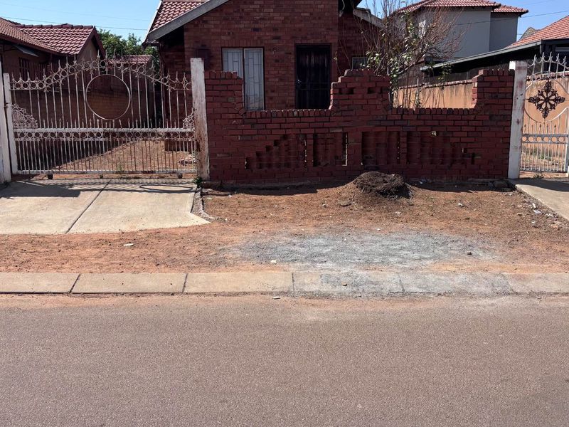Front exterior view of a brick house featuring a gated driveway, pedestrian entrance, and a front yard area requiring landscaping.