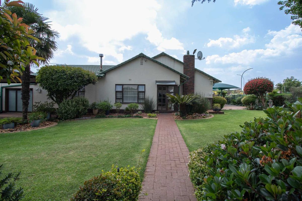 A well-maintained rear exterior view of the house featuring a brick pathway leading to the entrance, a landscaped garden, and a brick chimney.