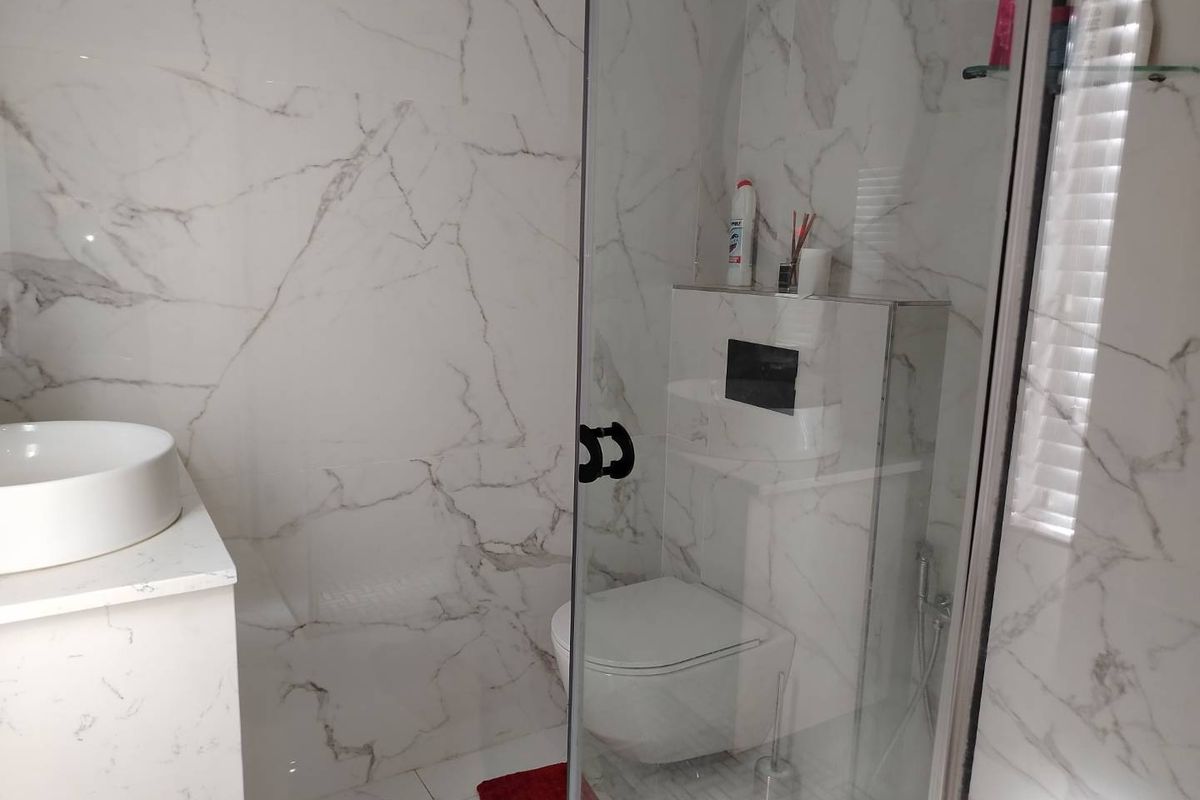 Modern bathroom featuring marble-look wall tiles, a wall-mounted toilet with a concealed cistern, and a glass-enclosed shower area.